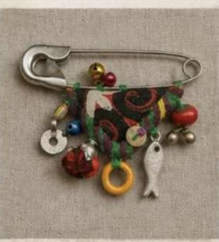 A safety pin brooch hung with beads, discs and a small brass fish